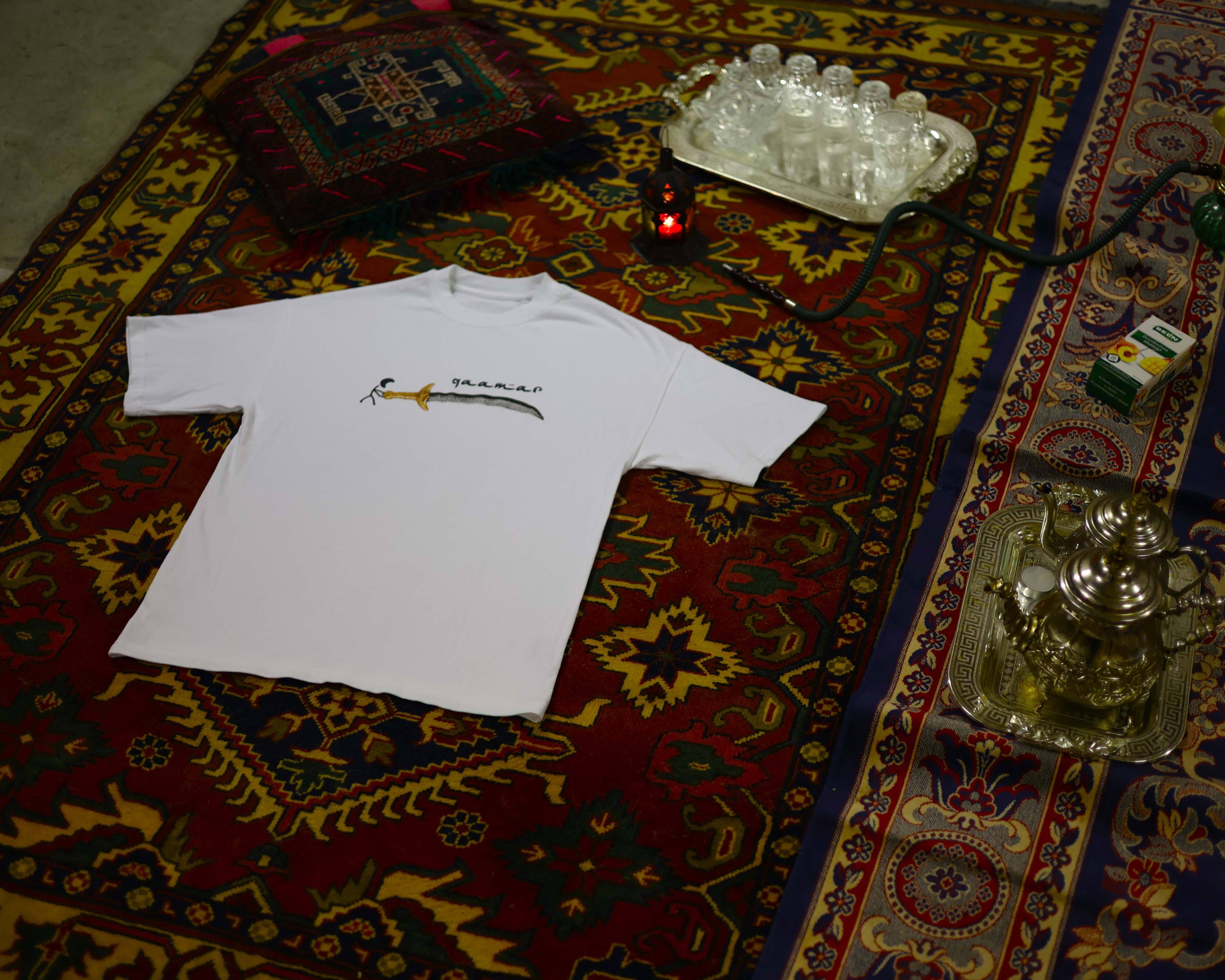 Photographie d'un t-shirt Qaamar posé sur un tapis